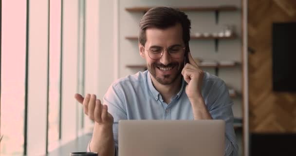 Feliz joven hombre de negocios llevando a cabo la llamada de teléfono celular, trabajando en la computadora. — Vídeo de stock