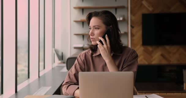 Distracted from computer work smiling businesswoman holding mobile phone conversation. — Stock Video