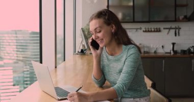 Mutlu yetenekli genç iş kadını telefonla konuşuyor, bilgisayarla çalışıyor..