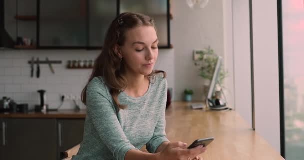 Relaxed young smiling woman using smartphone in modern kitchen. — Stock Video