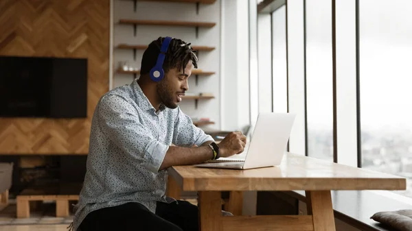 Young african guy use headphones laptop make notes of webinar — Stock Photo, Image