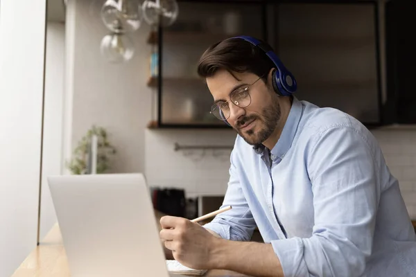 Homem atento no fone de ouvido olhar na tela do PC tomar notas — Fotografia de Stock