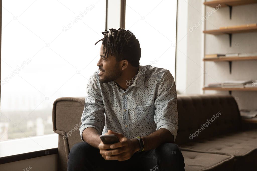 Happy african guy look at window with smartphone in hands