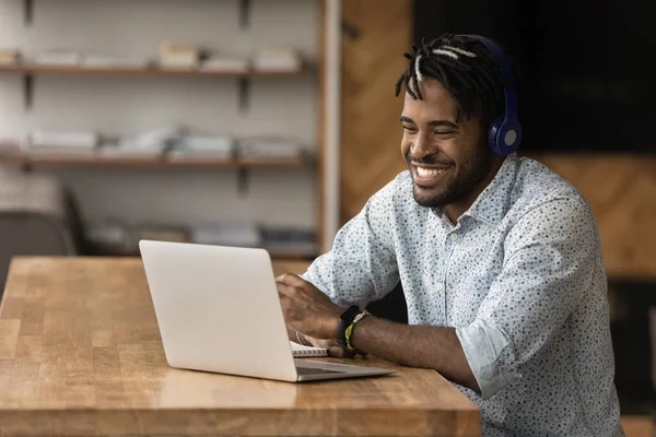 Laughing millennial afro guy in earphones relax by pc screen — Stock Photo, Image