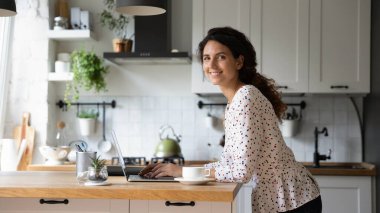 Evde dizüstü bilgisayarda çalışan gülümseyen kadın portresi.
