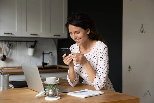 Mujer sonriente distraída forma trabajo de computadora utilizando el teléfono celular —  Fotos de Stock