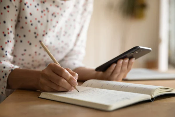 Primer plano del uso de la mujer celular escribir en el cuaderno —  Fotos de Stock