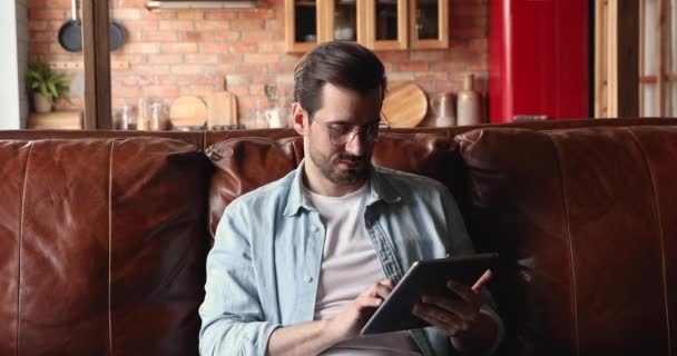 Millennial man sitta på soffa med tablett gadget — Stockvideo