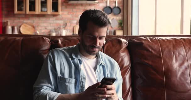 Mann sitzt mit Smartphone drinnen und verbringt Freizeit im Internet — Stockvideo