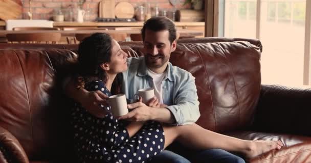Ζευγάρι χαλαρώνοντας στον καναπέ κρατώντας κύπελλα απολαύσετε ποτό και συζήτηση — Αρχείο Βίντεο