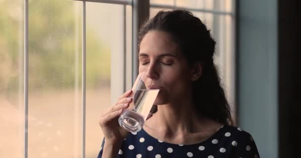 Ung kvinde holder glas drikkevarer naturligt vand stående indendørs – Stock-video