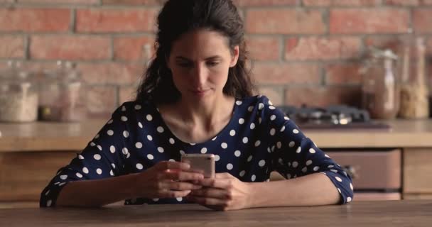 Улыбающаяся женщина сидит на кухне со смартфоном и покупает продукты онлайн — стоковое видео