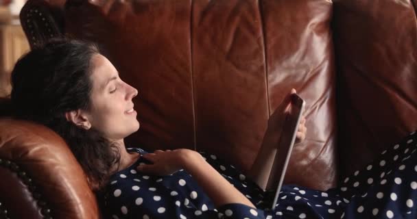 Розслаблена жінка лежить на дивані з планшетом сучасний пристрій — стокове відео