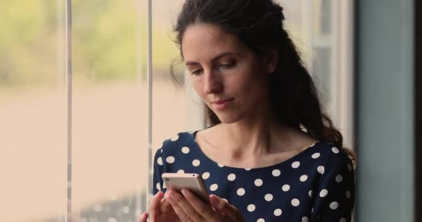 Mujer de pie cerca de la ventana en casa usando teléfono inteligente — Vídeo de stock