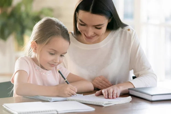 Glad ung mamma och liten dotter studerar hemma — Stockfoto