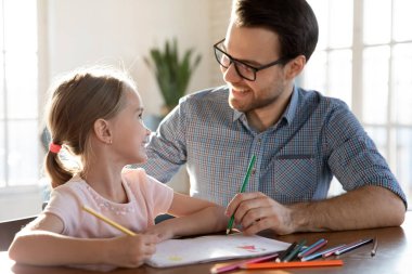 Gülümseyen baba ve küçük kız birlikte çiziyorlar.