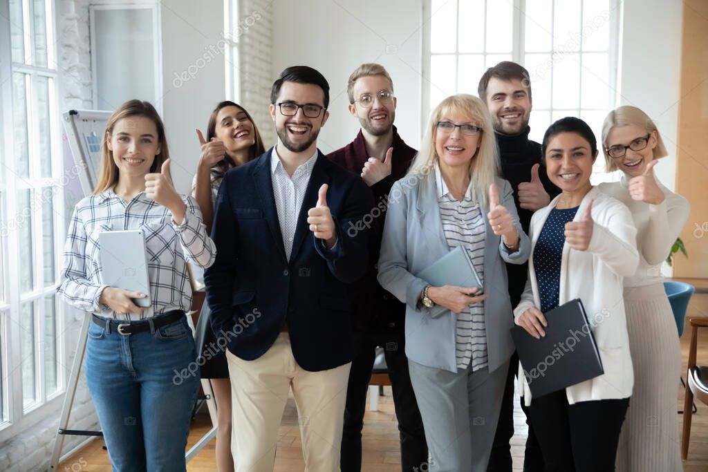 Portrait of successful mature businesswoman and team showing thumbs up