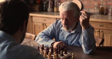 Düşünceli orta yaşlı adam yetişkin oğluyla satranç oynuyor..