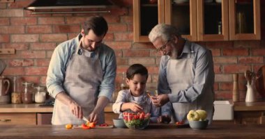 Neşeli üç erkek nesil önlüklü aile birlikte yemek pişiriyor..