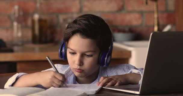 Petit garçon ciblé d'âge scolaire dans des écouteurs étudiant à distance. — Video