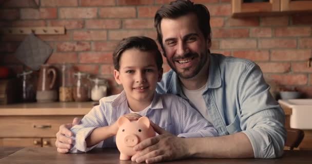Счастливый молодой отец и маленький сын откладывают деньги на будущее. — стоковое видео