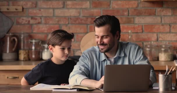 Sonriente padre joven ayudando a su pequeño hijo con la tarea. — Vídeos de Stock