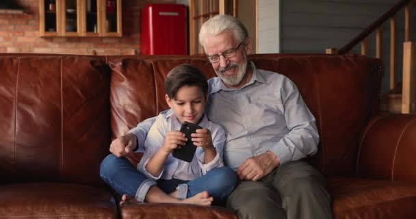 Liefdevolle oude grootvader kijken kleine jongen spelen op smartphone. — Stockvideo