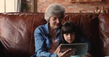 Büyükanne ve torun kanepede dinlenmek için tablet kablosuz cihaz kullanıyorlar.
