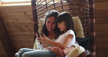 Küçük kız ve anne akıllı telefonlarıyla salıncakta dinleniyorlar.