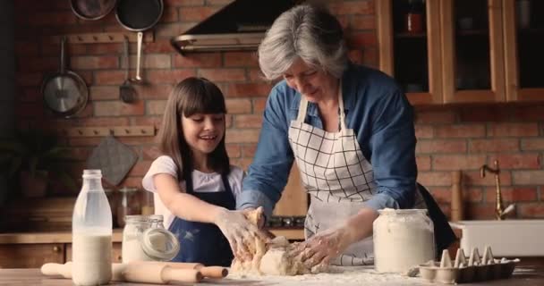 Elderly 60s granny preparing dough with little granddaughter — Stock Video