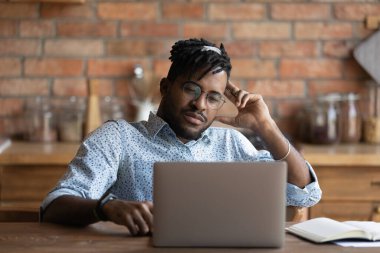Düşünceli Afrikalı Amerikalı adam dizüstü bilgisayar ekranına bakıyor.