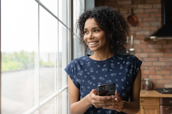 Nahaufnahme einer verträumt lächelnden Afroamerikanerin mit Smartphone — Stockfoto