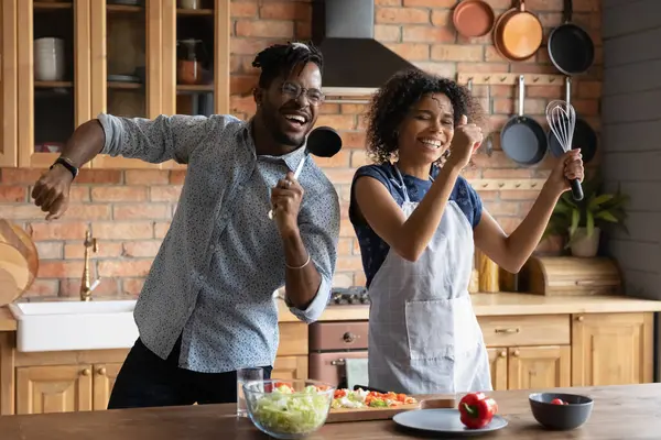 Close up overjoyed pareja afroamericana cantando en utensilios de cocina —  Fotos de Stock