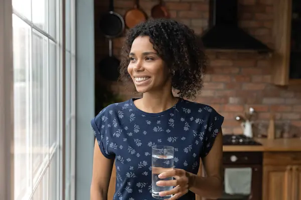 Close up dreamy African American woman holding glass of water — Stock Photo, Image