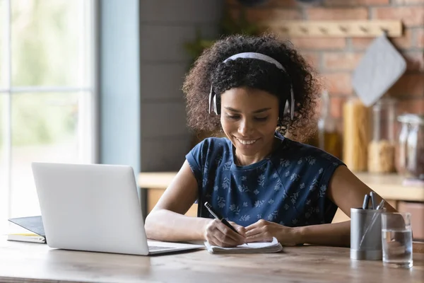 Close up smiling African American woman in headphones taking notes — Stock Photo, Image
