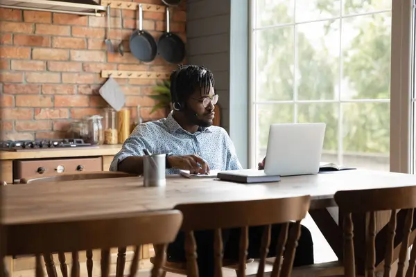 Confident African American man wearing headset using laptop in kitchen — Stock Photo, Image