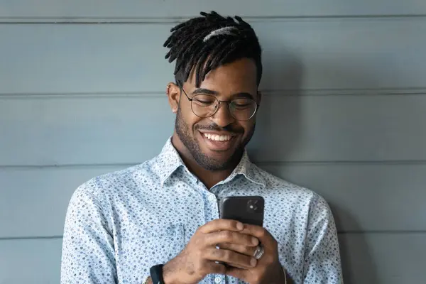 Närbild leende afroamerikansk man bär glasögon med hjälp av telefon — Stockfoto