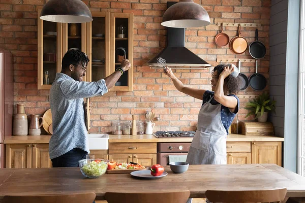 Pareja afroamericana divertida fingiendo luchar con utensilios de cocina, divirtiéndose —  Fotos de Stock