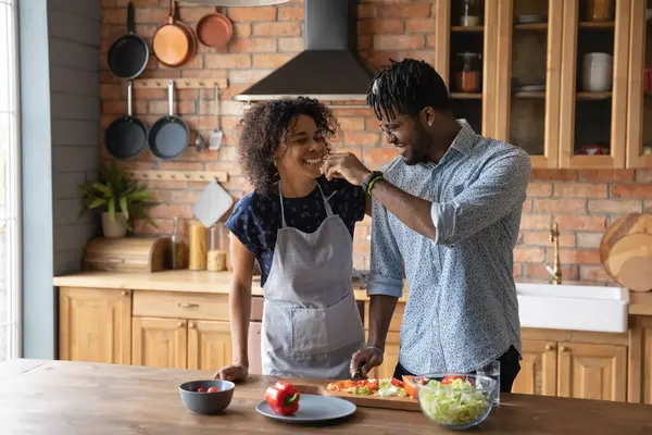 Feliz hombre afroamericano alimentando esposa, cocinando ensalada juntos —  Fotos de Stock