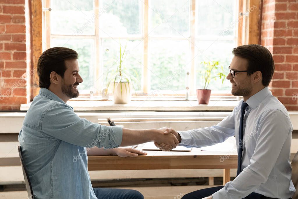 Smiling business partners shake hands greeting at meeting