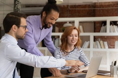 Gülümseyen çok ırklı çalışanlar ofiste bilgisayarda birlikte çalışıyorlar.