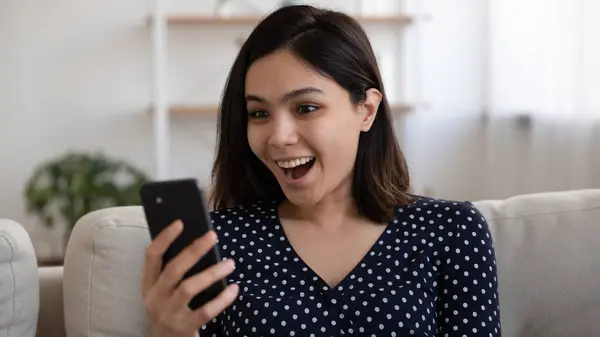 Jovem asiático feminino olhando para o telefone espantado com agradável surpresa — Fotografia de Stock