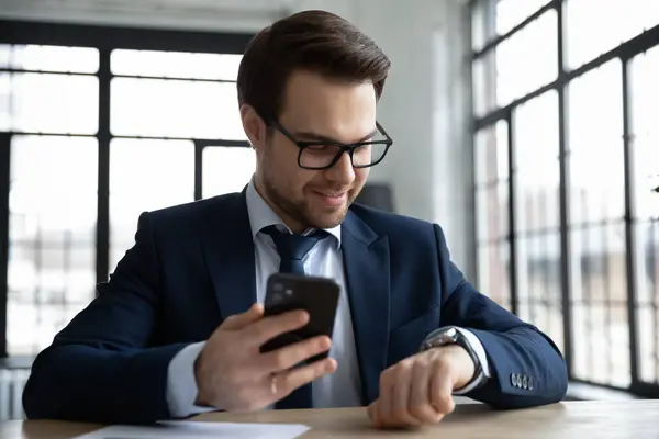 Leende affärsman använder mobiltelefon och smartwatch på arbetsplatsen — Stockfoto