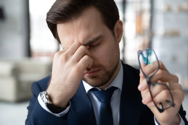 Empregado masculino exausto sofre de dor de cabeça no local de trabalho — Fotografia de Stock