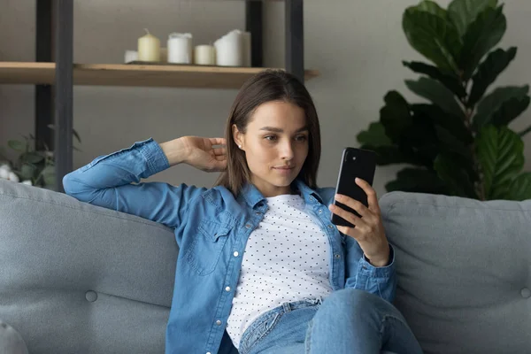 Bastante hembra sentada en el sofá sosteniendo smartphone posando para selfie — Foto de Stock