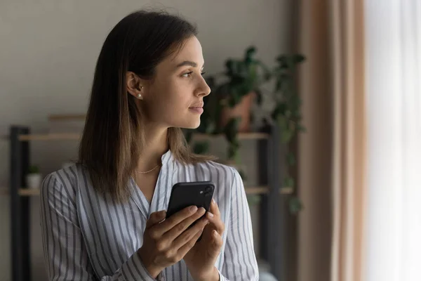 Aufmerksame junge Frau hält Handy zur Seite — Stockfoto