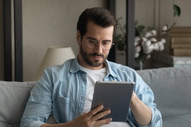 Ciddi milenyum erkeği kanepede oturup Pad Screen 'e bakar.