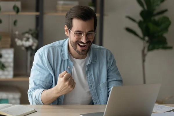 Щасливий студент чоловічої статі сидить за комп'ютером святкувати хороший результат іспиту — стокове фото