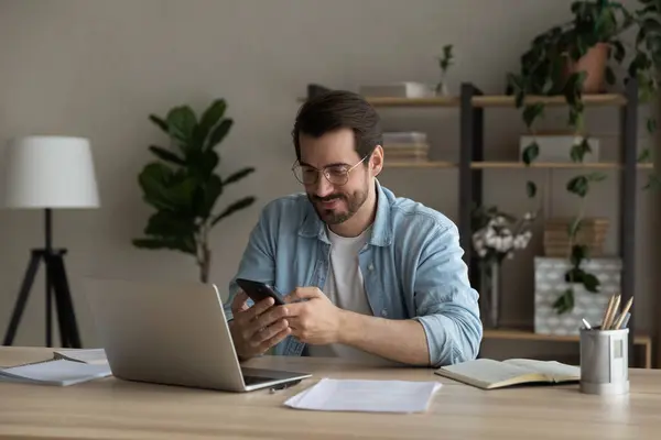 笑顔の若い男は、ホームコンピュータとスマートフォンの間でデータを同期 — ストック写真