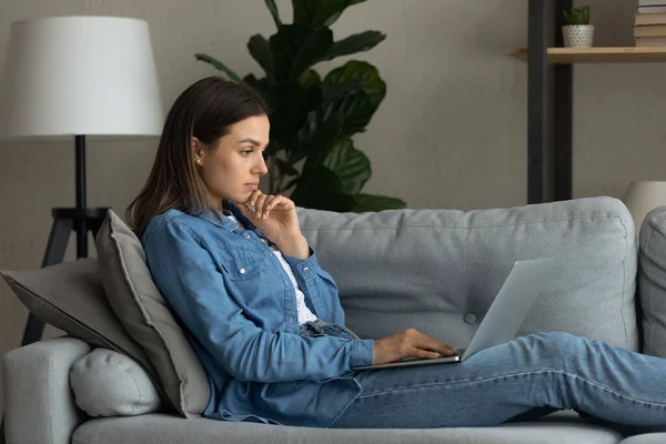 Pensive mladá žena číst příspěvek na blogu na obrazovce notebooku — Stock fotografie